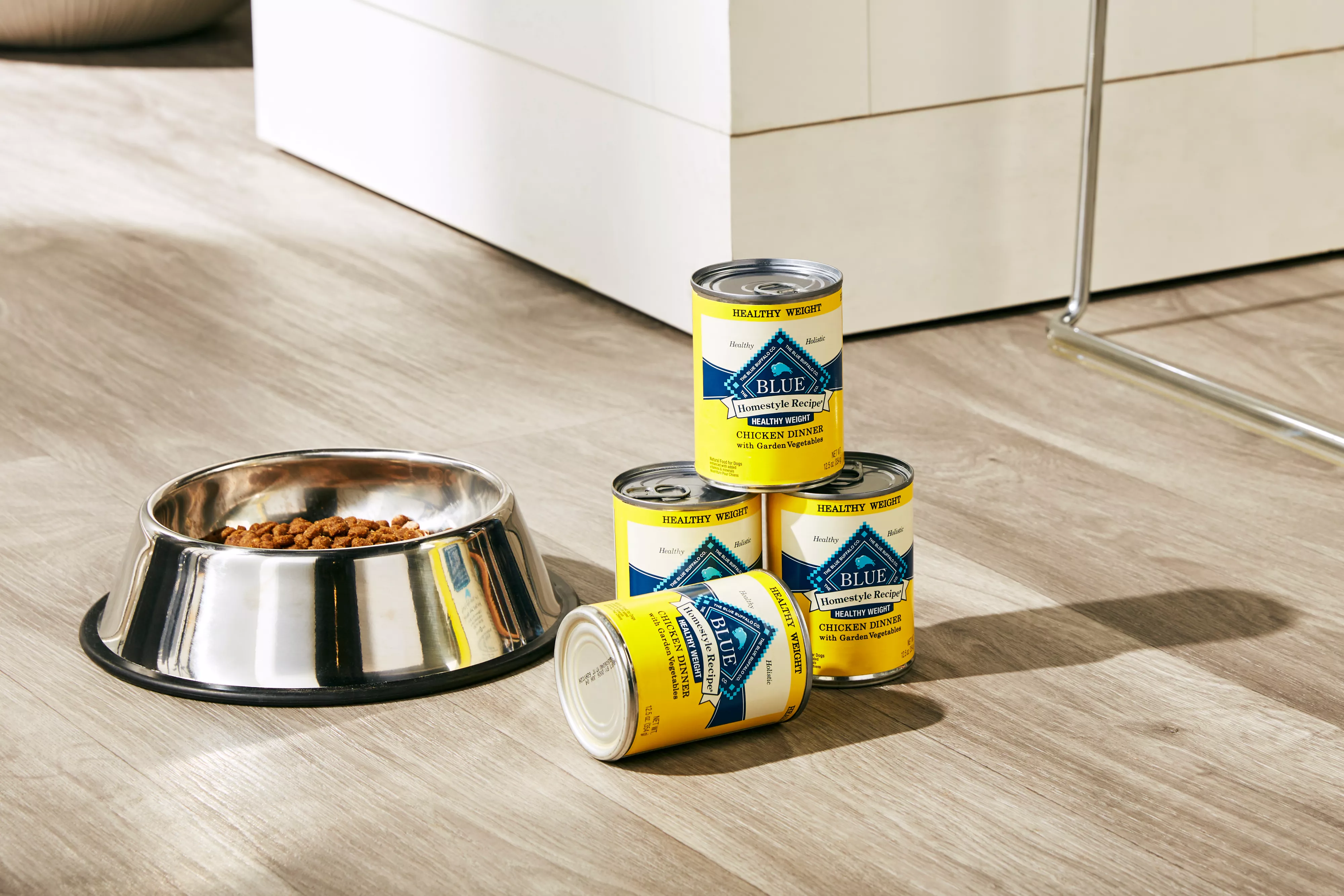 Four cans of Blue Buffalo Homestyle Recipe Healthy Weight next to a dog food bowl